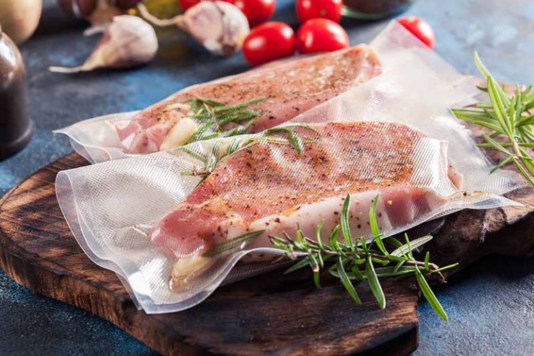 Horizontal image of sealed thick slices of raw pork with herbs on a wooden board.
