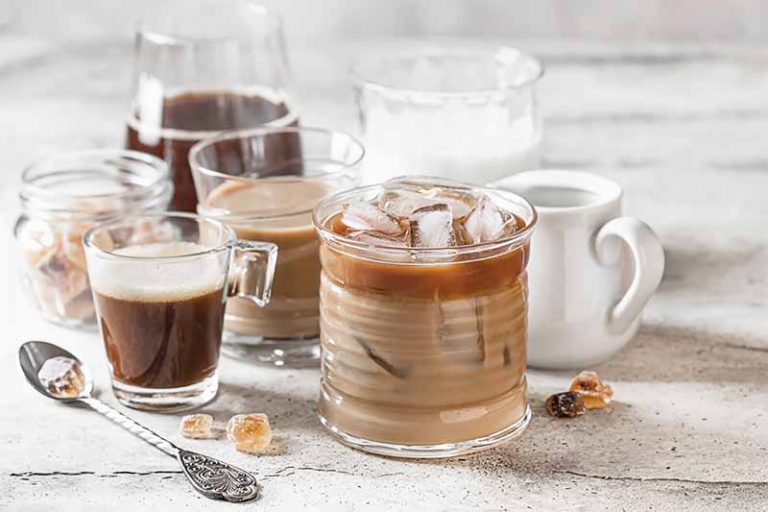 Horizontal image of assorted glasses and mugs filled with beverages and ice cubes.