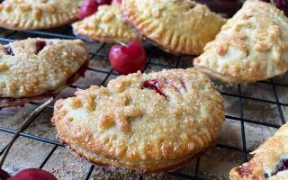 Horizontal image of assorted mini half-moon pastries filled with a red filling on a cooling rack.