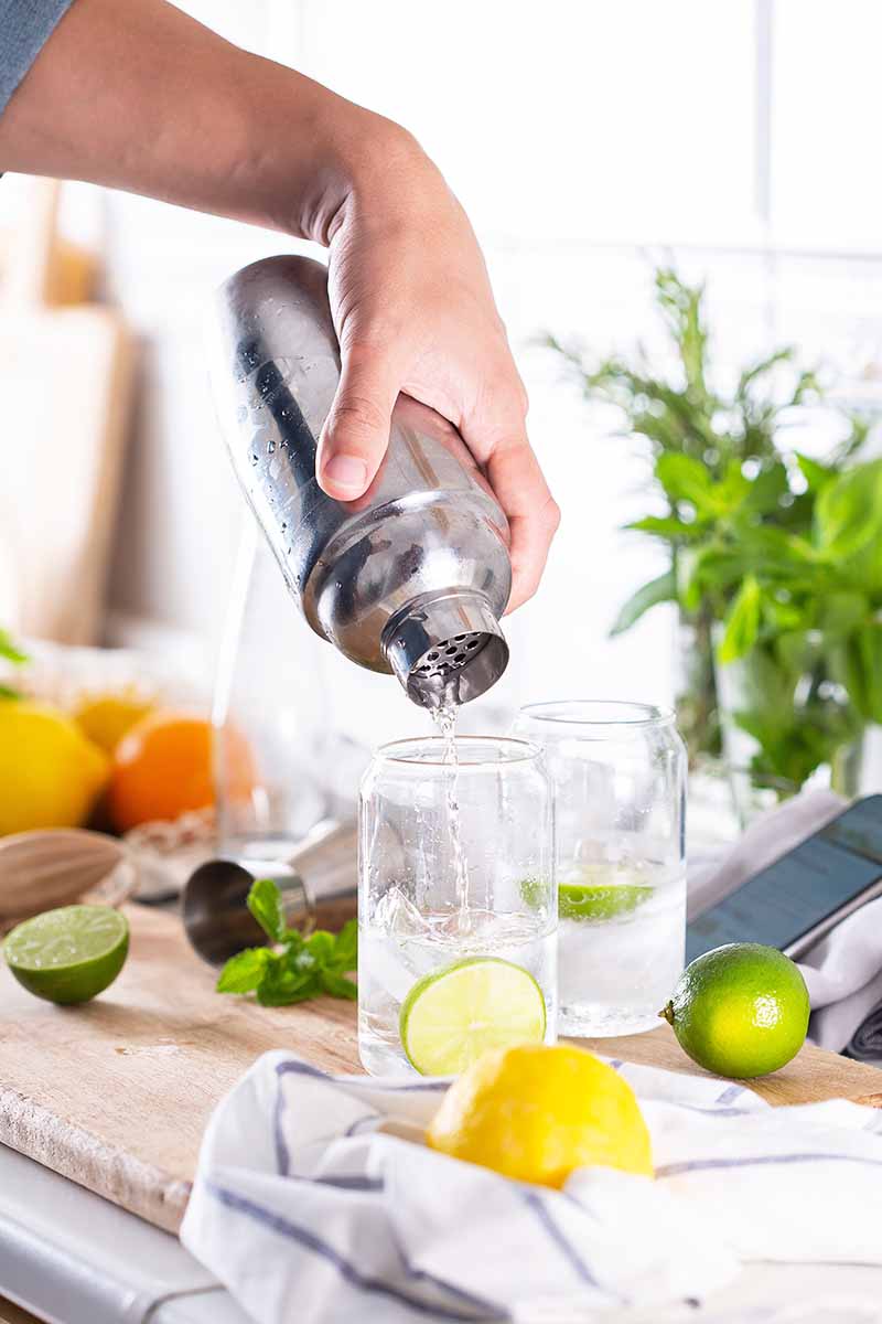 Vertical image of a man pouring out liquid into a clear cup on a counter next to ingredients.