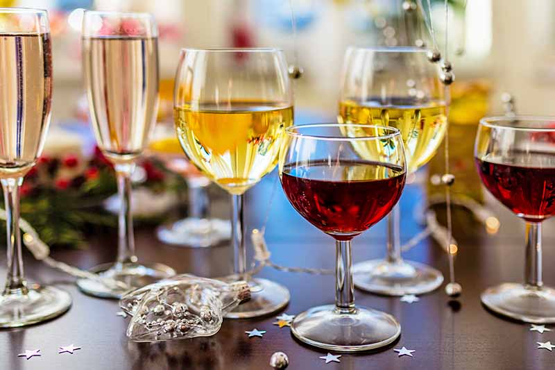 Horizontal image of three pairs of champagne, white, and red wine glasses, filled with the appropriate beverages, on a brown table with plastic and foil star decorations.