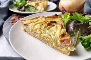 Horizontal image of a slice of savory pie on a plate next to salad greens.