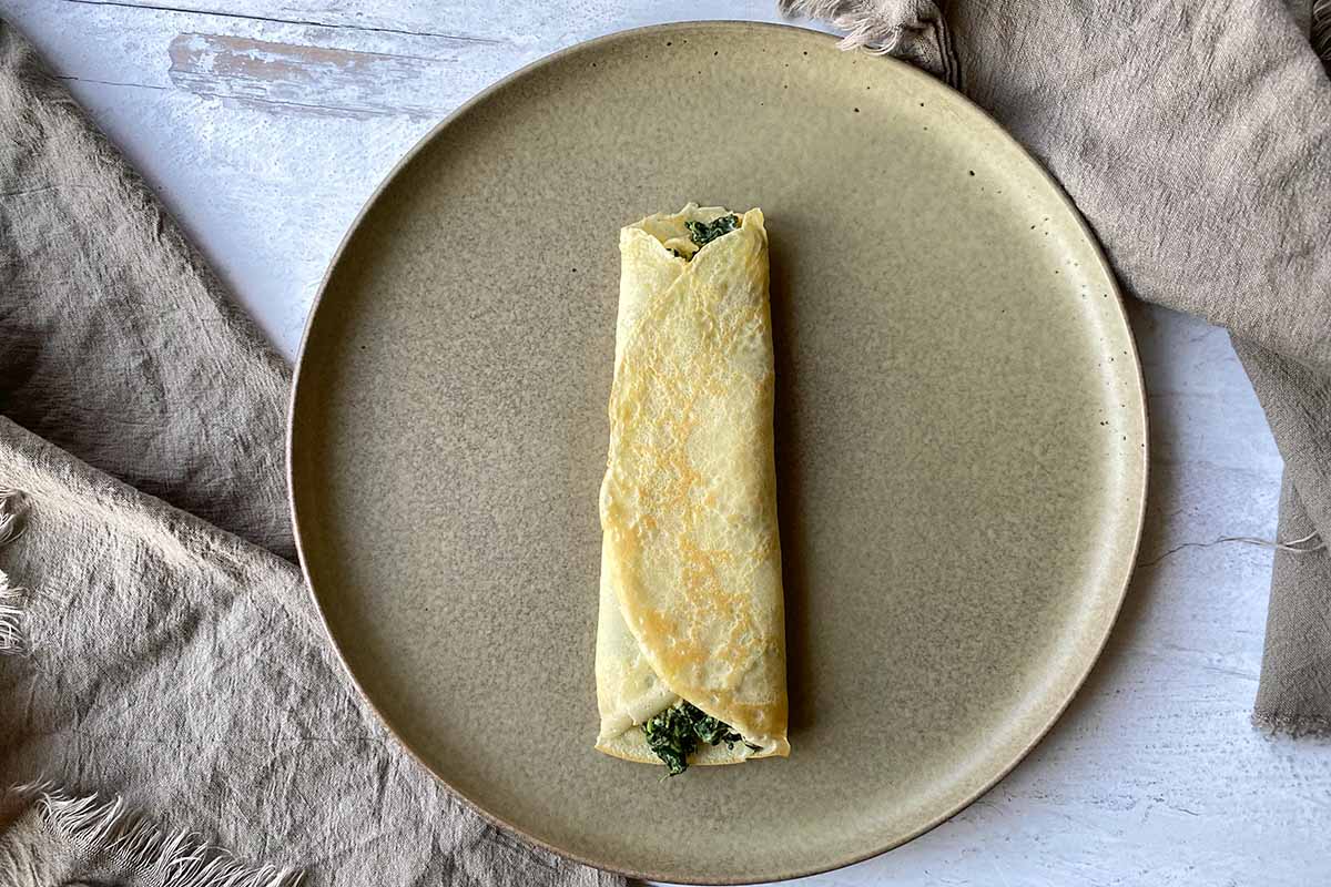 Horizontal image of a folded thin pancake with a creamy greens mixture inside on a plate.