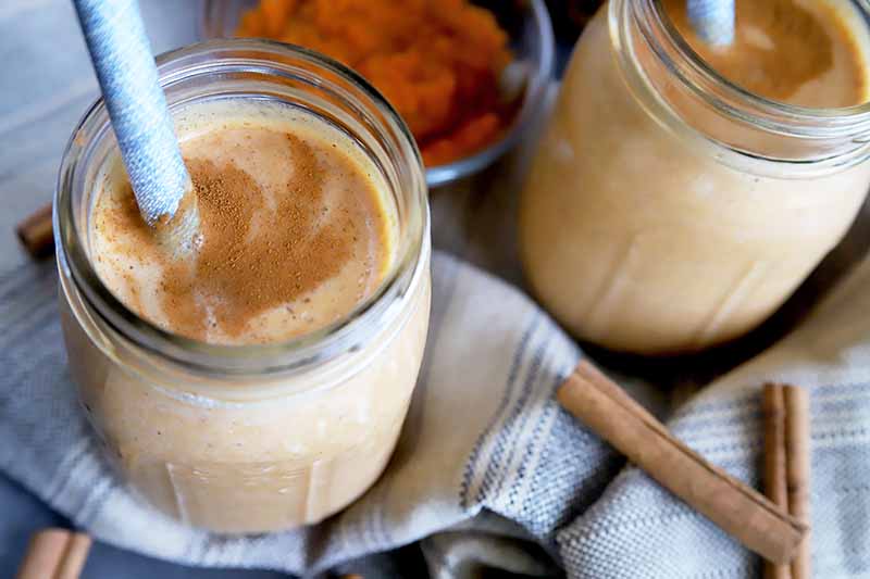 Horizontal image of two mason jars filled with a light orange creamy liquid with straws.