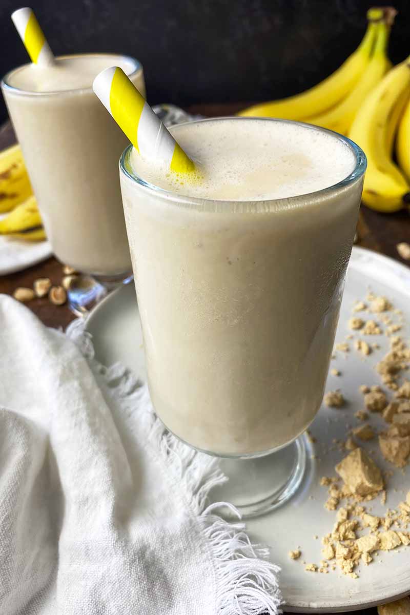 Vertical image of two glasses filled with a creamy tan beverage with yellow straws inserted to them.