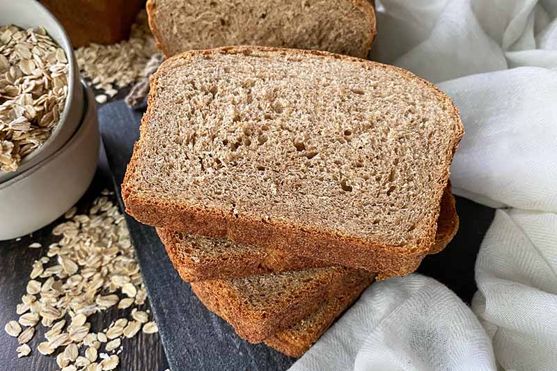 Horizontal image of a stack of bread slices on a gray table next to oats and a white towel.
