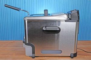 The T-fal Ultimate EZ Clean Fryer sitting on a butcher board table with a medium blue background.