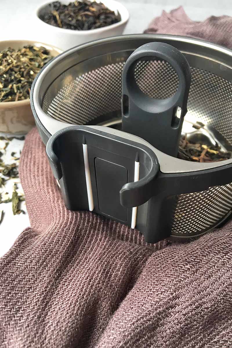 Vertical image of a tea basket with its magnetic attachment on a brown towel.