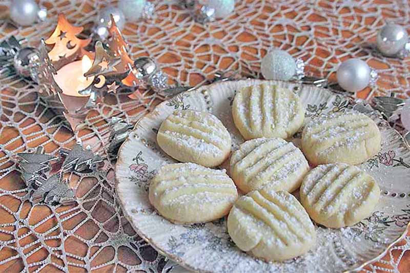 Horizontal image of a plateful of small round baked goods surrounded by winter decor.