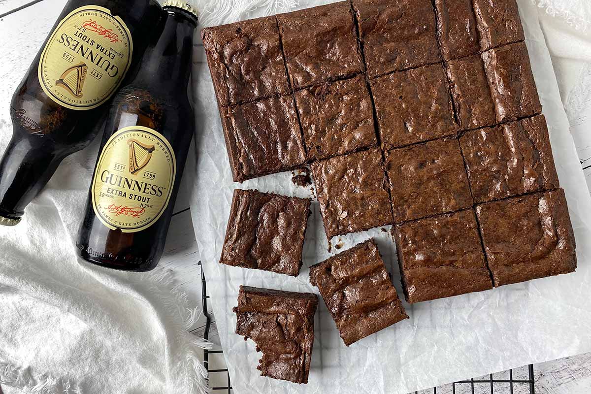 Horizontal image of portioned individual square baked goods on a parchment paper next to bottles of beer.