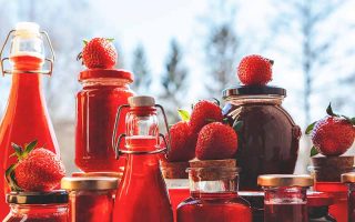 Horizontal image of assorted glasses and jars filled with a bright red sauce.