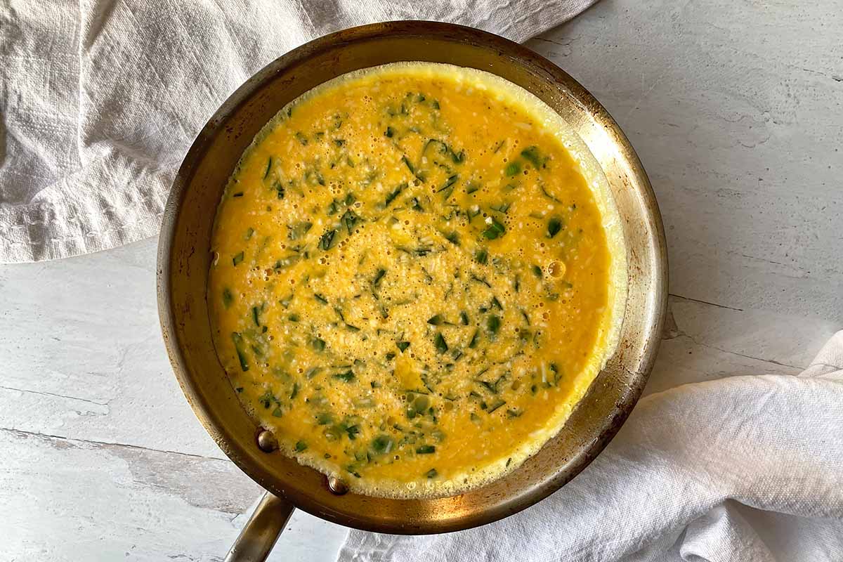 Horizontal image of an unbaked egg dish with chopped basil and cheese in a pan.