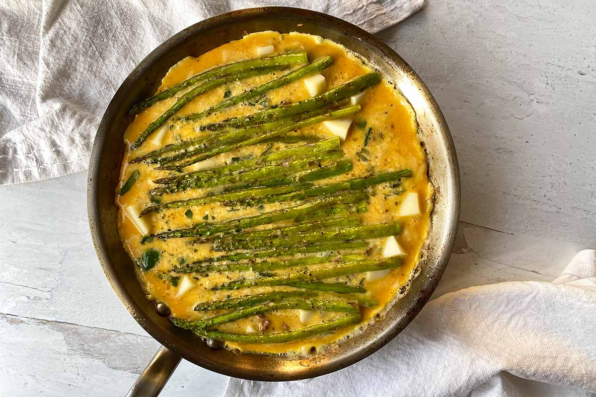Horizontal image of an unbaked egg dish in a pan topped with cheese cubes and vegetables.