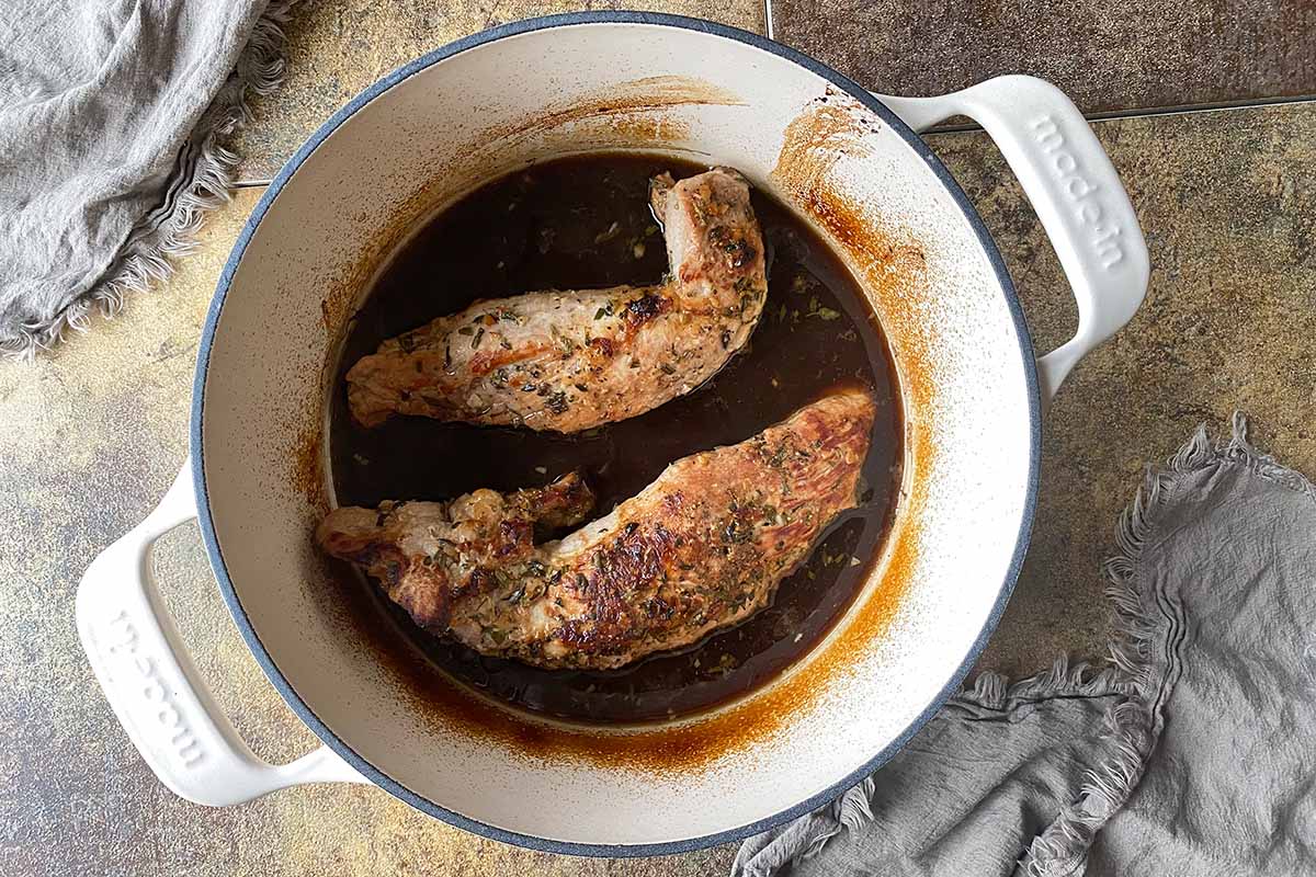 Horizontal image of two pieces of meat cooked in a dark liquid in a Dutch oven.