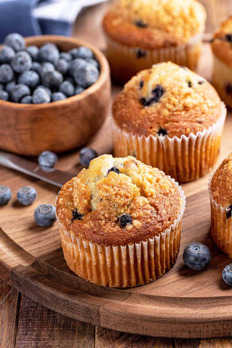 Vertical image of blueberry pastries on a wooden platter next to fresh blueberries.