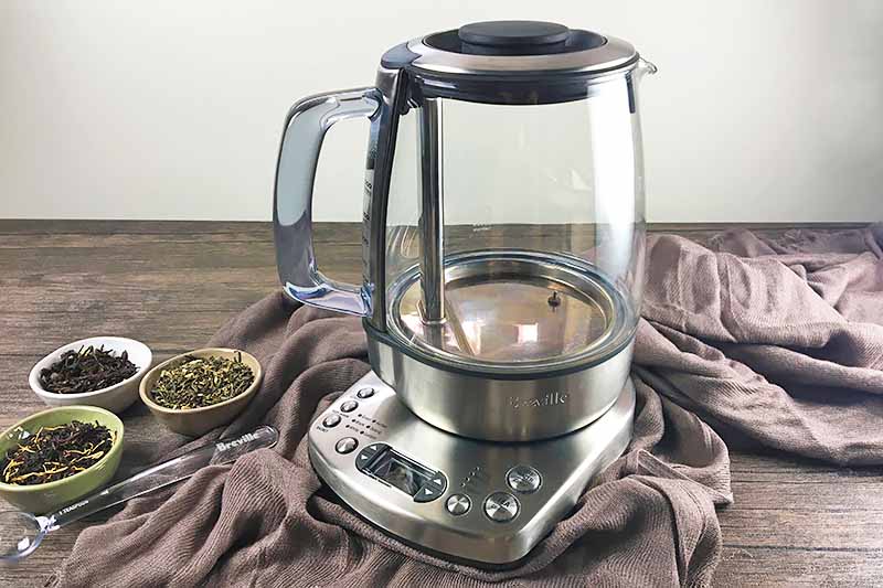 Horizontal image of a tea kettle and power base on a brown towel on a brown wooden table.