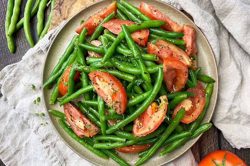 Horizontal top-down image of vibrant assorted vegetables mixed with herbs on a brown plate on top of tan towels.