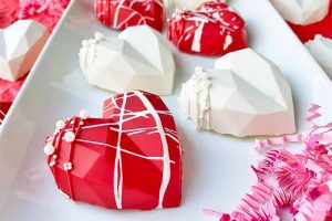 Horizontal image of decorated red and white chocolate shells on a white plate next to pink confetti.