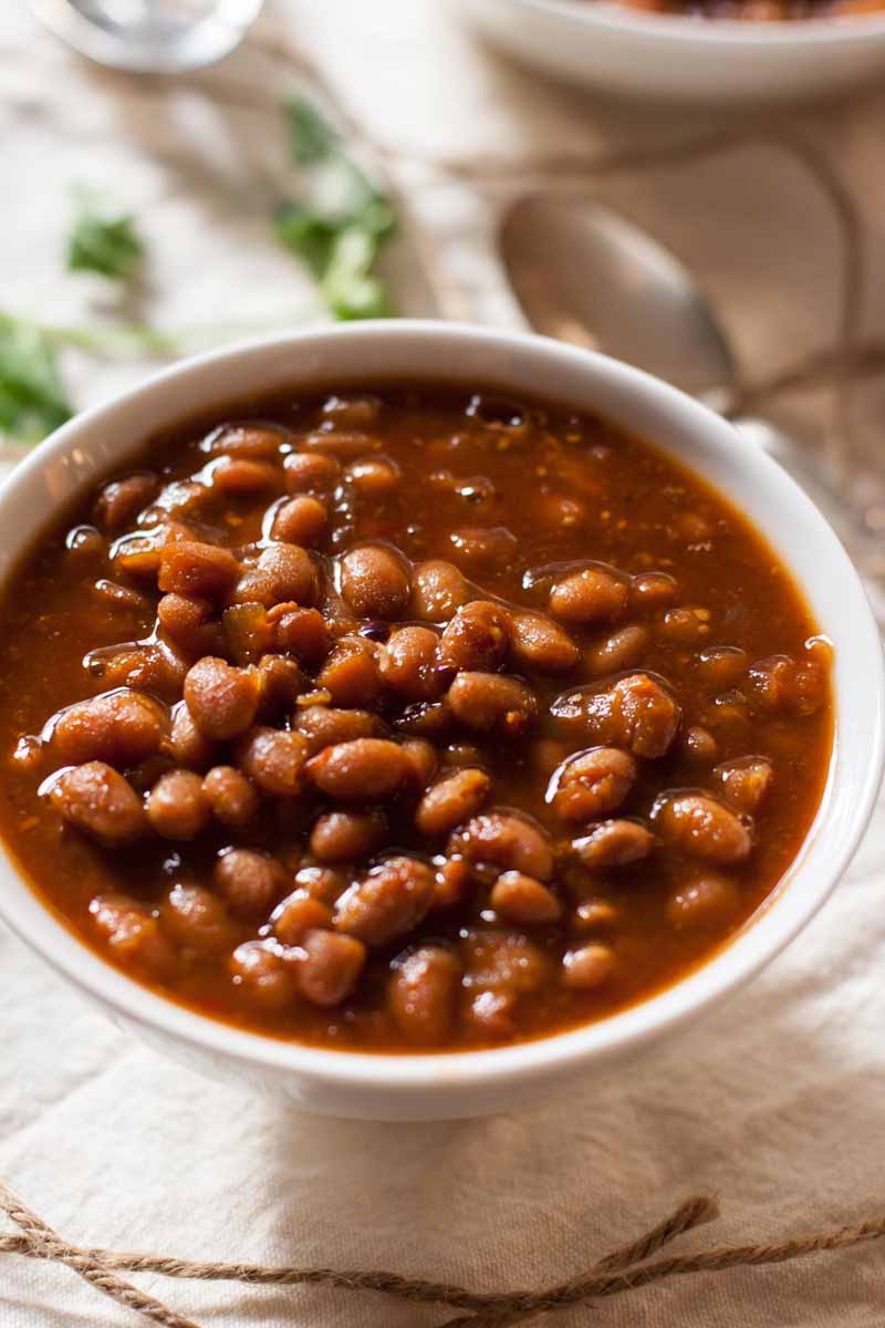 Oblique close up view of a white, ceramic bowl full of vegetarian slow-cooker baked beans.