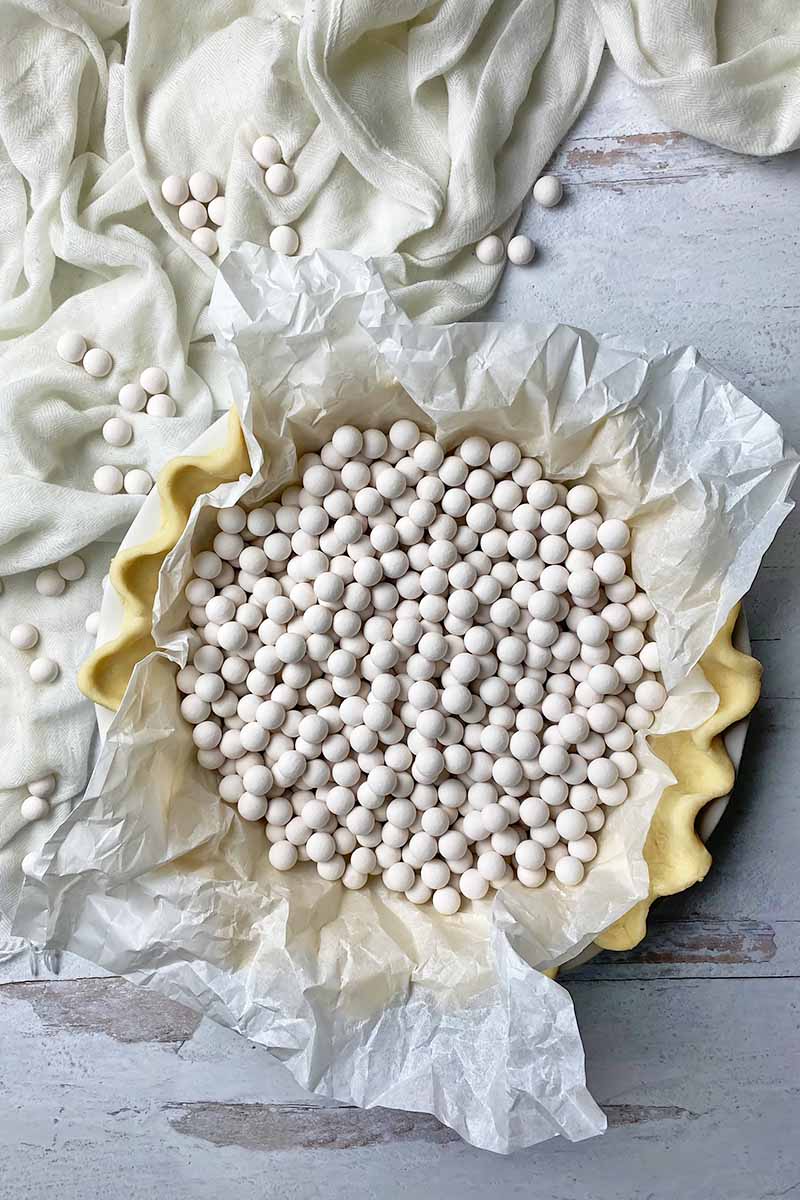 Vertical image of a raw formed pastry shell topped with a paper liner and ceramic white beads.