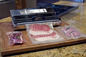 A photo of the Weston Pro 2300 vacuum sealer bagging cold cuts and other lunch meat on a large wooden cutting board.