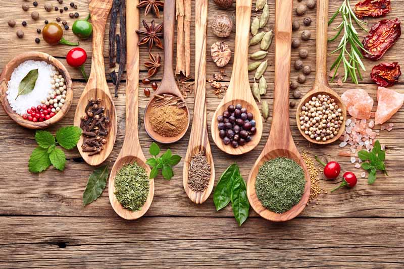 Top down view of seven wooden spoons and couple of bowls sitting on a rustic wooden table top and filled with various herbs and spices.